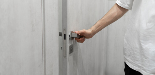 A persons hand is captured as it grasps a sleek, contemporary handle, preparing to open a light grey door.