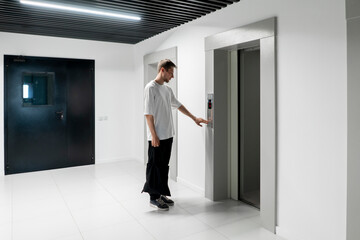 A young man stands poised to press the elevator call button in the sleek hallway of a contemporary...