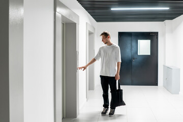 A young man stands poised to press the elevator call button in the sleek hallway of a contemporary...