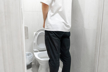 back view of Man Standing in Bathroom, urinating into a toilet.