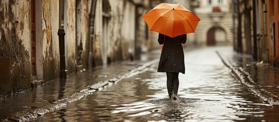 Stylish woman with orange umbrella walking on flooded street Stylish female in coat with umbrella walk on city street in rainy day Alone female with umbrella. Copy space image. Place for adding text