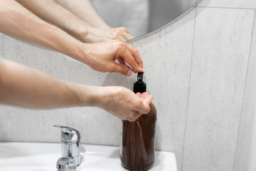 A person is seen using a dark-colored soap dispenser to apply liquid soap into their palm against a...