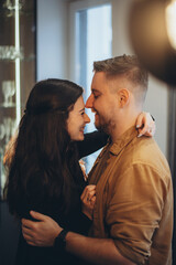 A married couple, a guy and a girl, stand opposite each other and smile. The girl hugs the guy by the neck.