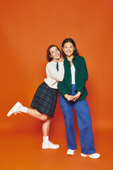 happy young multicultural women in vibrant casual attire posing together on orange background