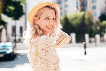 Young beautiful smiling blond woman in trendy summer yellow dress. Sexy carefree woman posing in the street  at sunset. Positive model outdoors at sunny day. Cheerful and happy. In hat