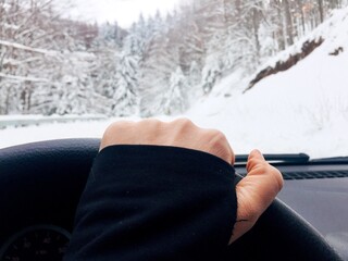 Hand on the steering  wheel and snowy road seen from the car windshield 
