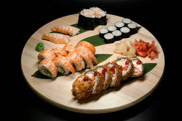 Set of sushi rolls lying on banana leaves on a round wooden board