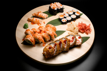 Top view of a set of sushi rolls decorated with banana leaves on a round wooden board
