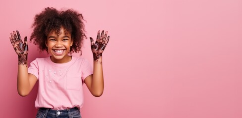 portrait beautiful afro american child girl dressed in t-shirt and smiling showing painted hands, pink light background - Powered by Adobe