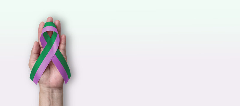 Green purple awareness ribbon for Stickler Syndrome and Anal cancer, anus health and illness awareness month with bow color on hand support on white background with copy space