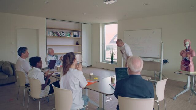 medical doctors attending a meeting for a clinical skills refresher applaud and cheer for colleague