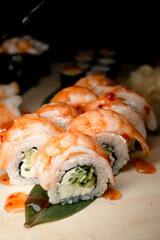Side view of shrimp rolls coated in glossy sauce with cucumber filling and cream cheese on banana leaf