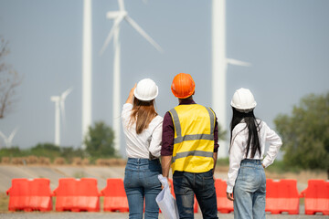 Back view of group engineers and architects on construction site with wind turbines in background