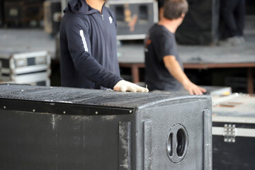 
Technicians working on setting up the stage for an event with music and lights. Men placing sound speakers for a musical show. Setting up live show scenery.