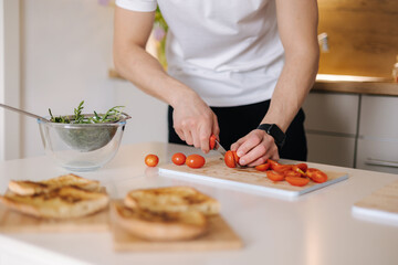 Handsome man take and slice little organic tomatoes on wooden board. Red cherry tomato