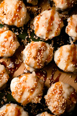 Focus on the foreground of baked sushi rolls with unagi sauce, sesame