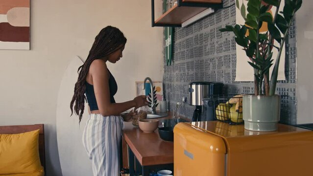 Full medium side shot of young African American girl in pajamas and with box braids preparing healthy breakfast in modern kitchenFull medium side shot of young African American girl in pajamas and wit