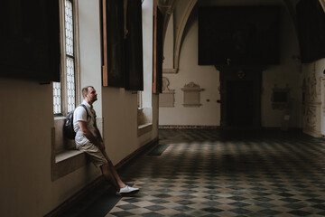 A man sits on a stone bench in an old castle and looks at the interior and ancient wall...