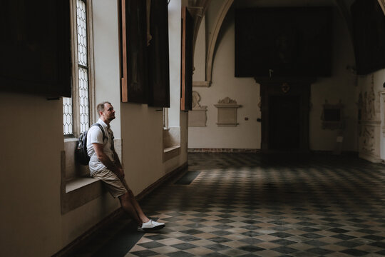 A man sits on a stone bench in an old castle and looks at the interior and ancient wall decorations. gallery with paintings. Museum visitor. High quality photography