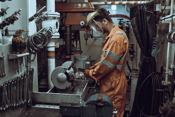 Young mechanical engineer repairing engine part, secured in vice in workshop, wearing coverall and goggles.