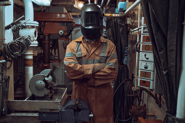 Standing portrait of welder wearing mask and orange coverall in workshop.