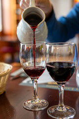 Pouring yound red beaujolais wine in glass during celebration of end of harvest and first sale release on third Thursday of November from white ceramic pitcher in Limouges, France