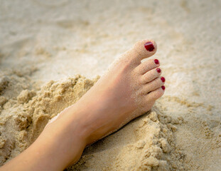 female foot with a red pedicure on the sand on the beach