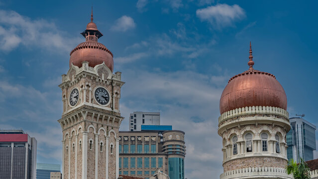 Details of the ancient architecture of Kuala Lumpur. Sultan Abdul Samad Building.   Clock towers, domes and spires on a background of blue sky and clouds. Modern skyscrapers in the distance. Malaysia