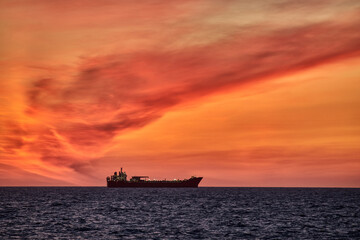Beautiful ocean sunset , with colourful red and orange sky, dark sea and silhouette of ship on the horizon.