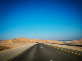 Highway through sand dunes. Highway in between mountains. Saudi Arabia's beautiful desert. Blue sky background 