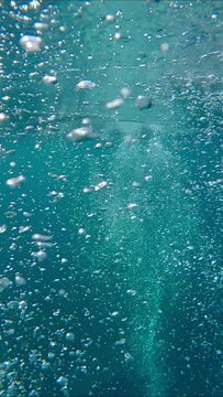 Vertical video, Air bubbles rise up to surface, slow motion. Bubbles of gas rise to surface from down of sea. Many air bubbles floating from sea bottom to water surface. Air bubbles in blue water