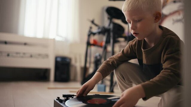 Close-up shot of a small albino boy with white hair puts a music record on the player and then turns it on and listens to music in his room. Antiques and hobbies of a little albino boy at home