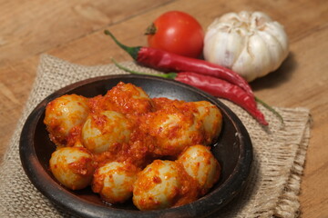 Telur Balado Tomat or Spicy Egg is traditional popular Indonesian food made from boiled egg with tomato and chili paste or sambal, served in earthenware plate on wooden table. Indonesian food. 