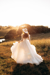 Fototapeta premium Luxury beautiful bride in a lush dress at sunset standing smiling.