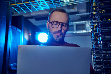 focused handsome professional in turtleneck with glasses and beard looking at his laptop, data