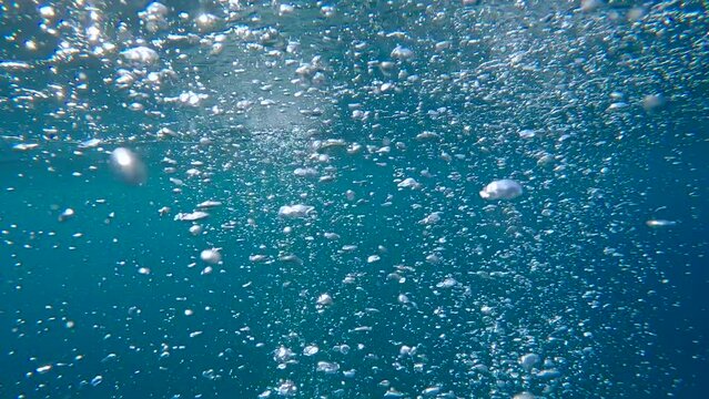 Close-up of air bubbles popping from the depths to the surface of the blue water, slow motion, Air bubbles rising in the turquoise water in the background