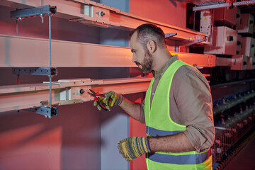 good looking pensive technician in safety vest and gloves working with pliers in data center