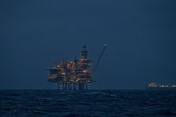 Close up view of illuminated drilling rig and floating production storage tanker at night in the...
