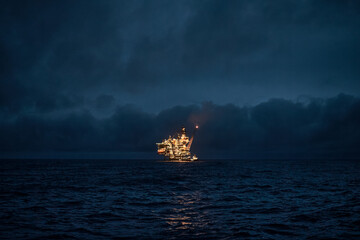 Panoramic view of offshore oil filed in the sea at night, with oil and gas drilling platform on the horizon.