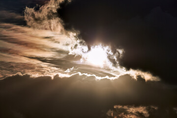 The sun shines through dark clouds creating beams of light in the air.