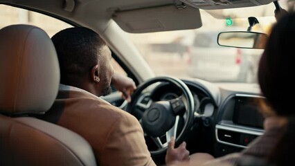 Rear view of a happy man Businessman with Black skin in a brown jacket rides in the car and drives the car during his business trip with a colleague brunette girl in the city