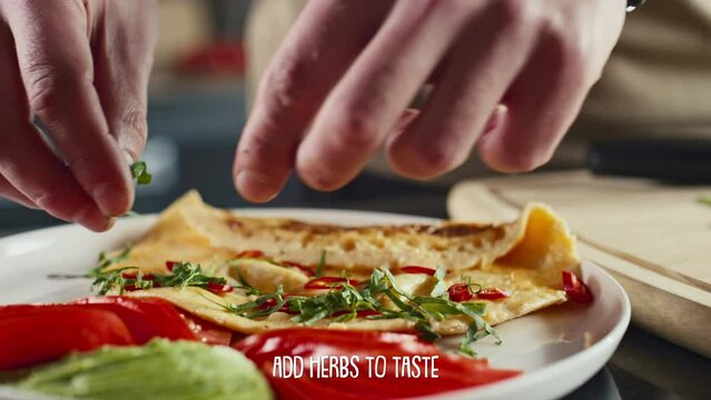 Hands of man adding chopped fresh herbs to omelet served on plate. Video recipe with subtitles describing cooking steps displaying below screenHands of man adding chopped fresh herbs to omelet served 