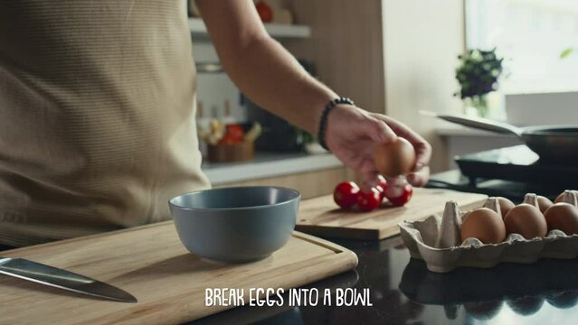 Close up shot of hands of male chef cracking eggs into bowl while making breakfast, subtitles describing recipe step appearing belowClose up shot of hands of male chef cracking eggs into bowl while ma