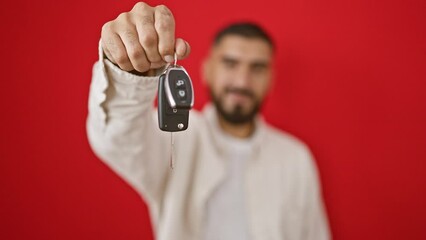 Smiling bearded man in white shirt holding car keys against red background epitomizes accomplishment and happiness.