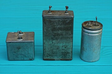 three old different electrolytic round and square aluminum dirty powerful large capacitors stand on...