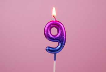 Pink and blue birthday candle burning on pink background. Number 9.