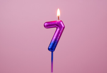 Pink and blue birthday candle burning on pink background. Number 7.