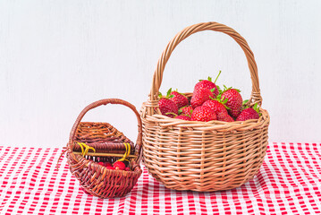 Fototapeta na wymiar Two wicker baskets with ripe strawberries and wild strawberries on a checkered tablecloth