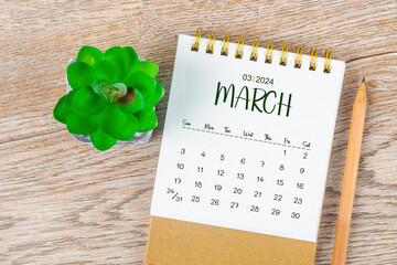 March 2024 monthly desk calendar and pencil with plant pot decoration on wooden background.
