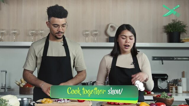 Two co-hosts in aprons standing in kitchen and telling about food ingredients on camera during TV cooking show, animated lower third displaying below screenTwo co-hosts in aprons standing in kitchen a